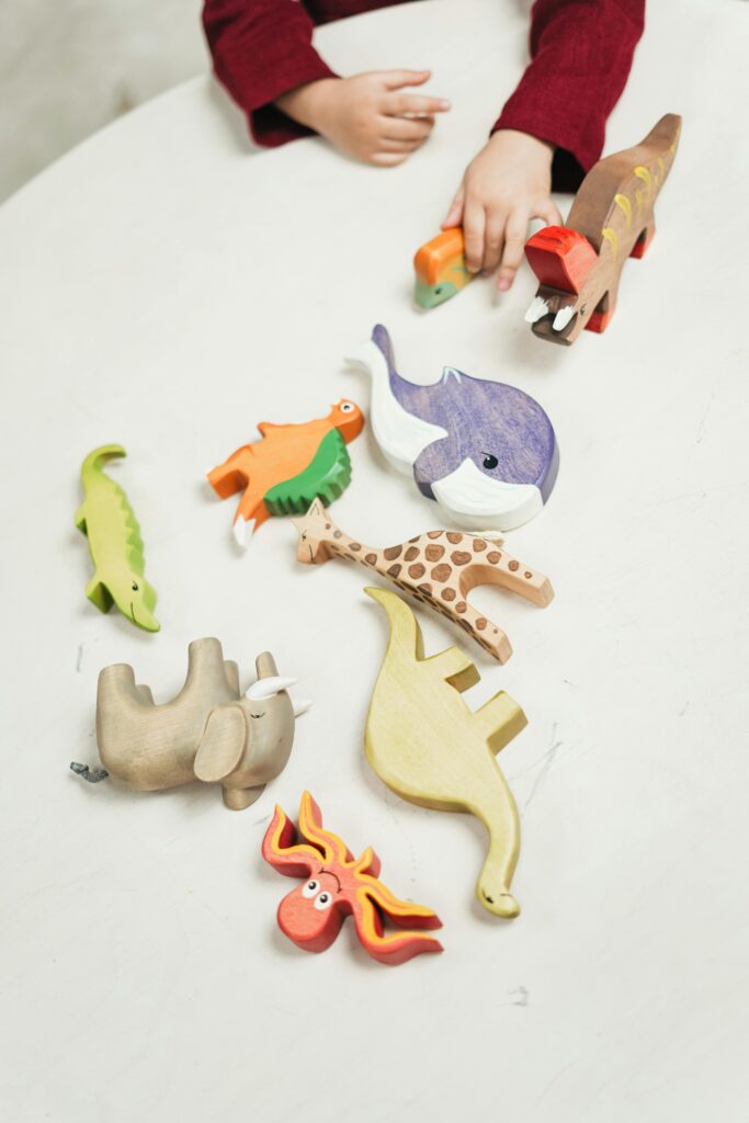pexels-photo-3662643-3662643 A child plays with a variety of colorful wooden animal toys on a white table indoors.