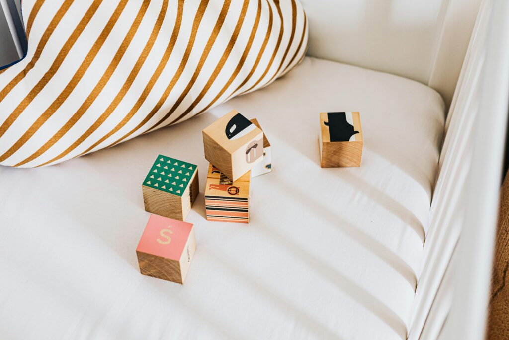 pexels-photo-4964374-4964374 A set of colorful wooden blocks on a white bed with a striped pillow.